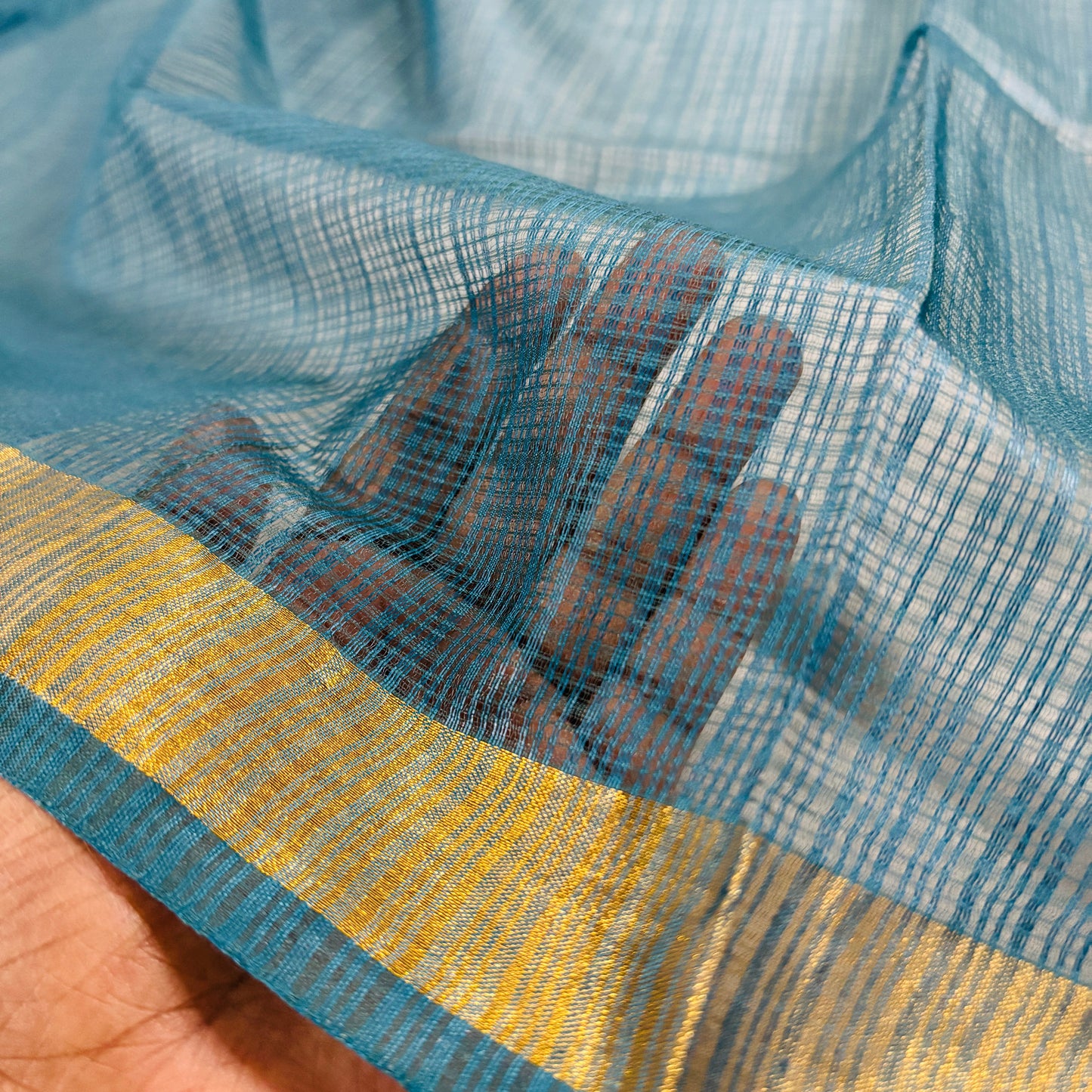 close up of Green kota doria silk saree with gold border on a grey background