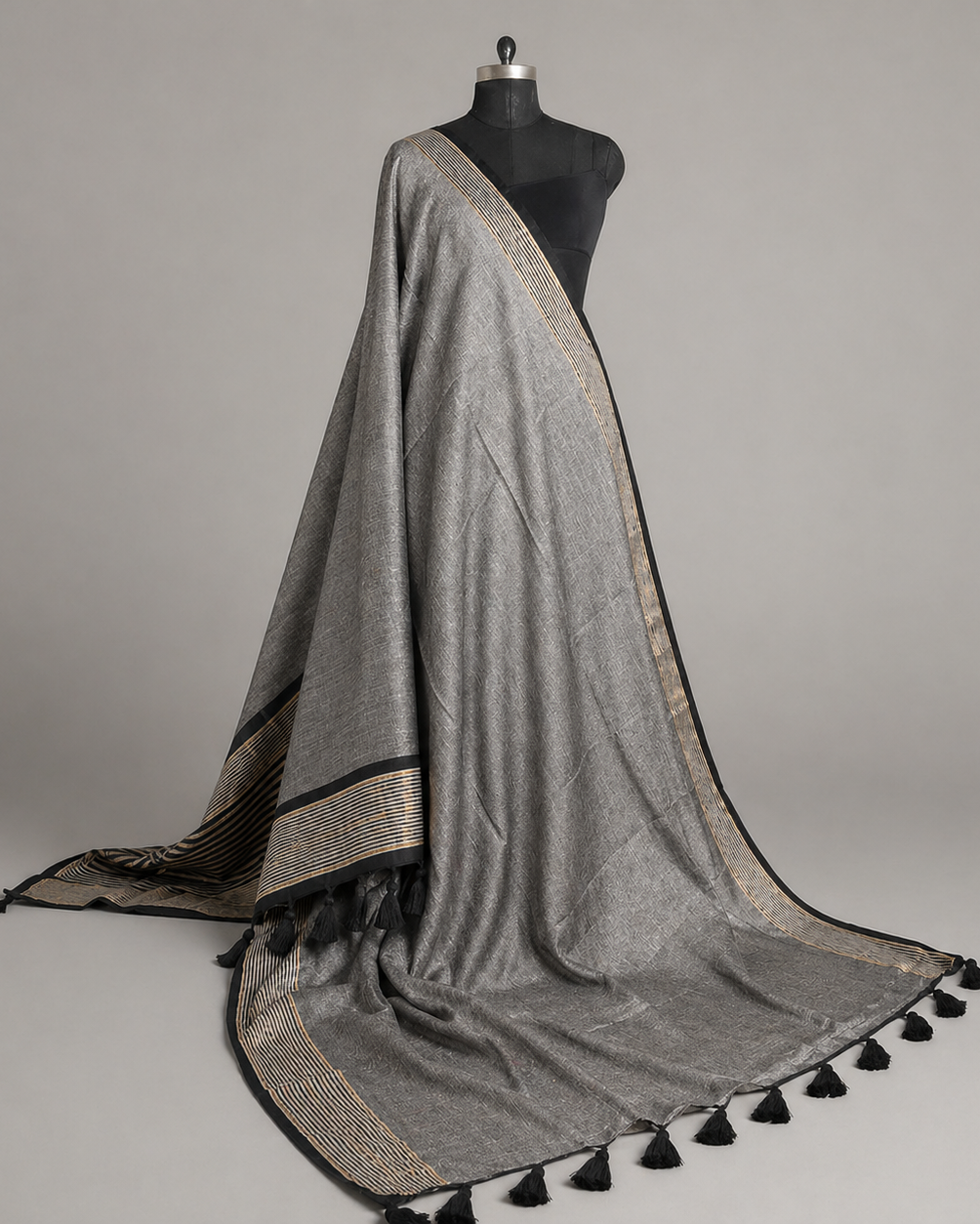Gray saree with black and gold striped pallu draped over a mannequin against a gray background