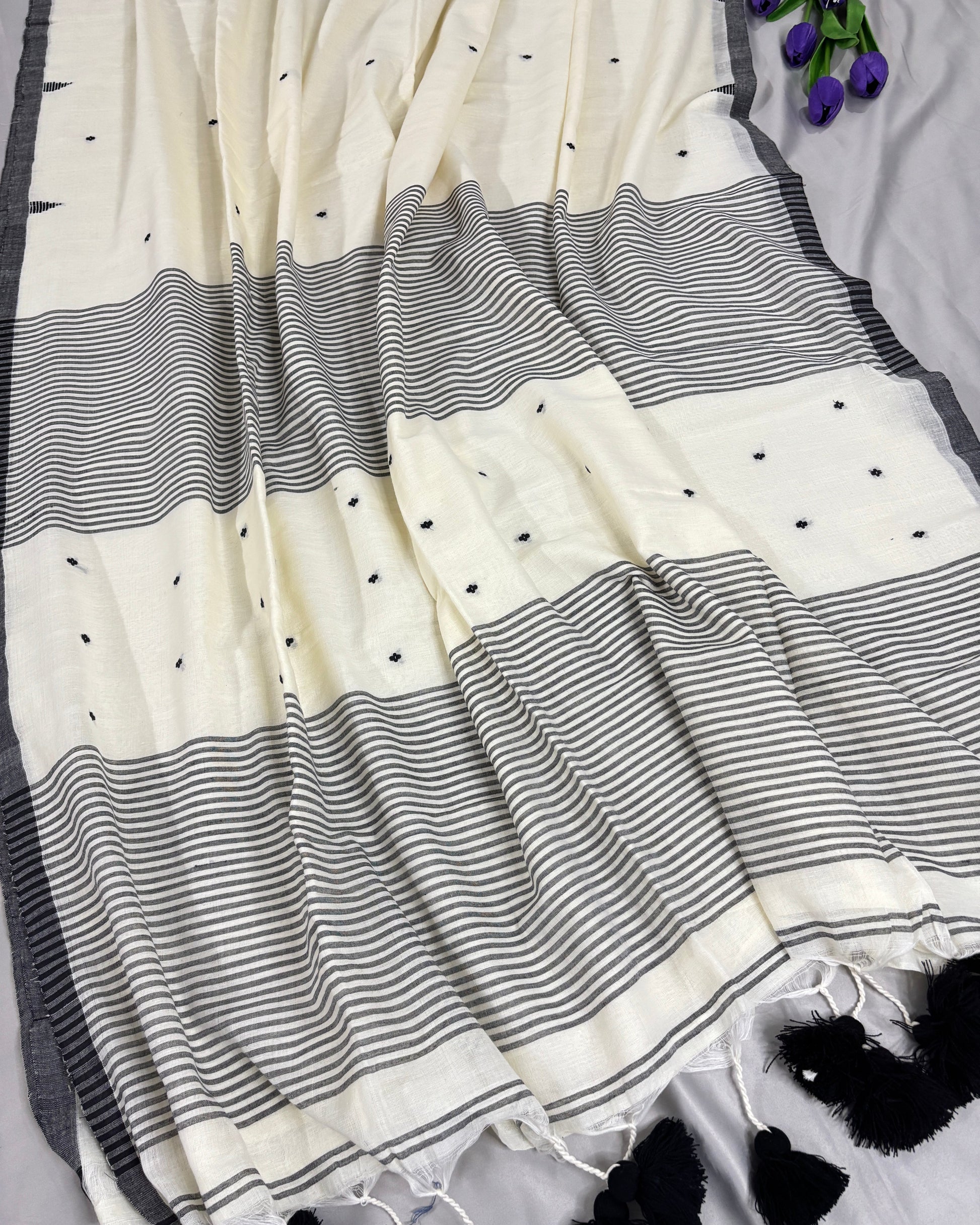 White saree with black temple border and tassel pallu on a gray surface