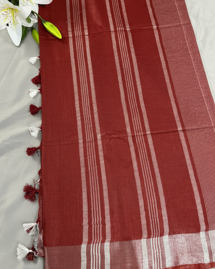 Rust Red linen saree with silver striped pallu and tassels on a gray background