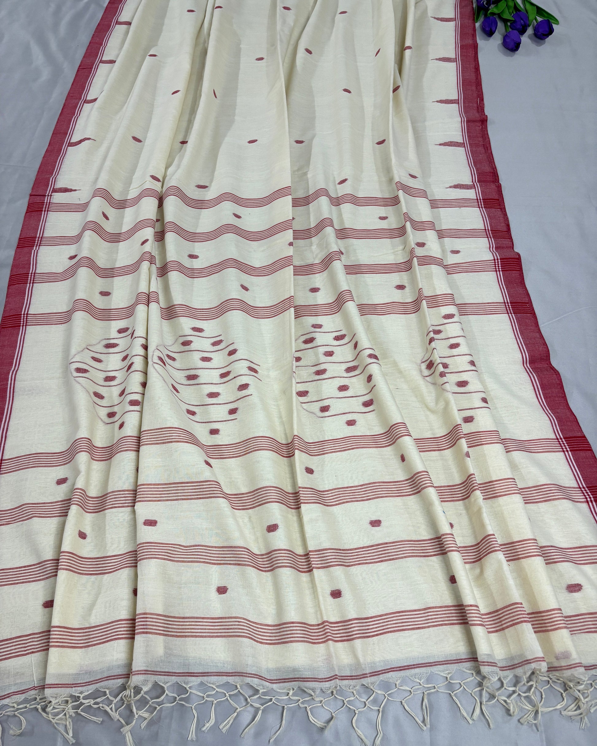 White Handloom cotton saree with red patterns on a grey background