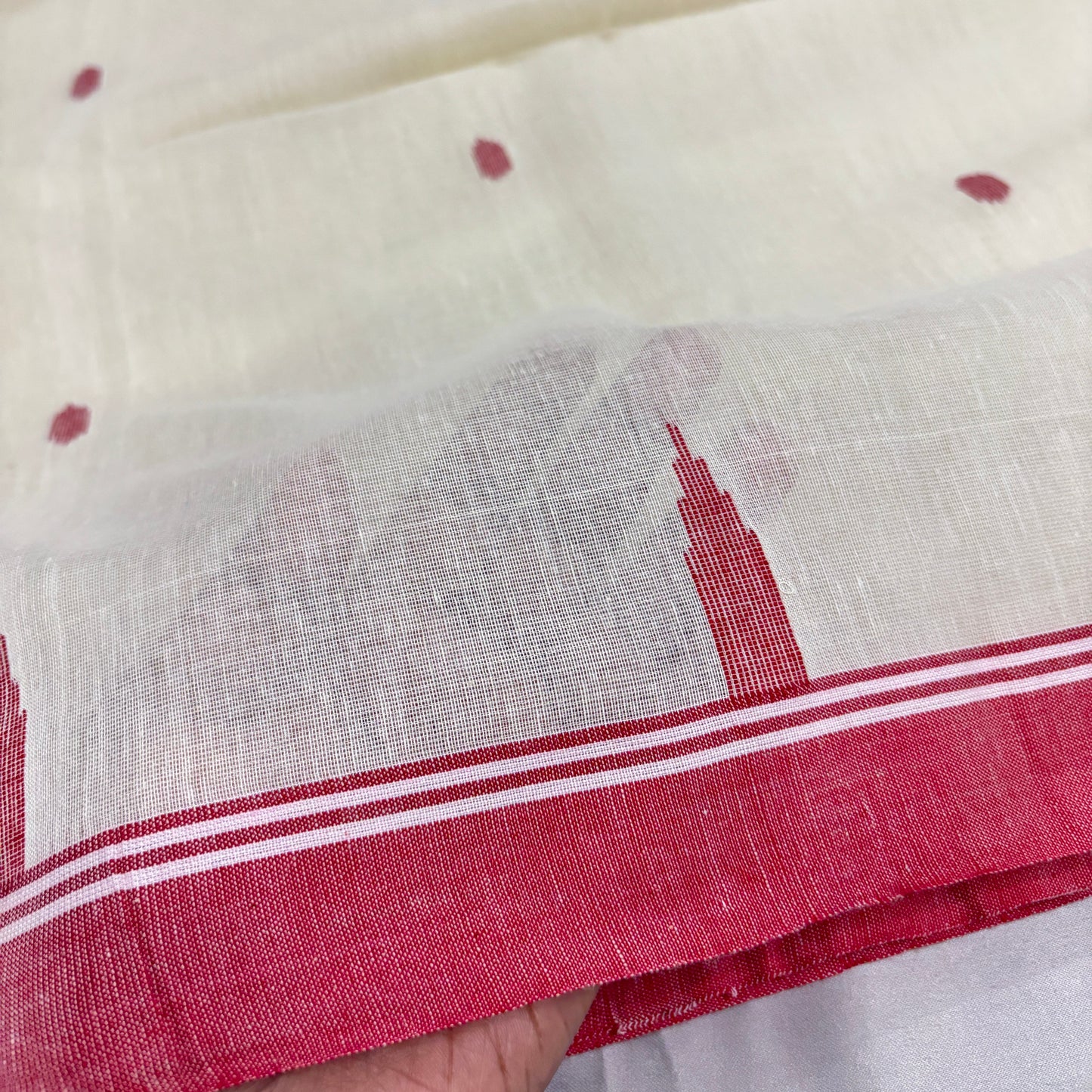 Close-up of a white cotton saree with red border held by a hand