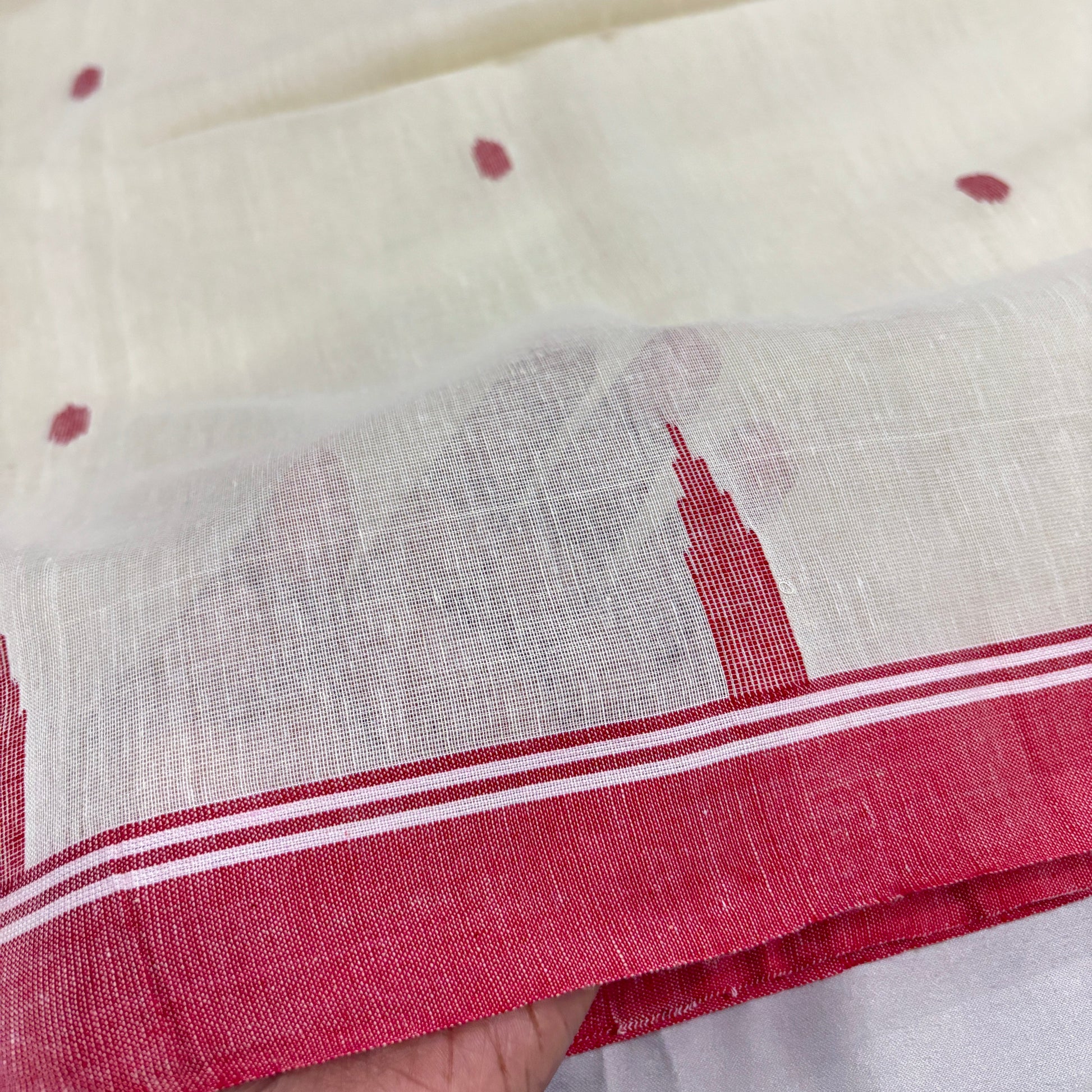 Close-up of a white cotton saree with red border held by a hand