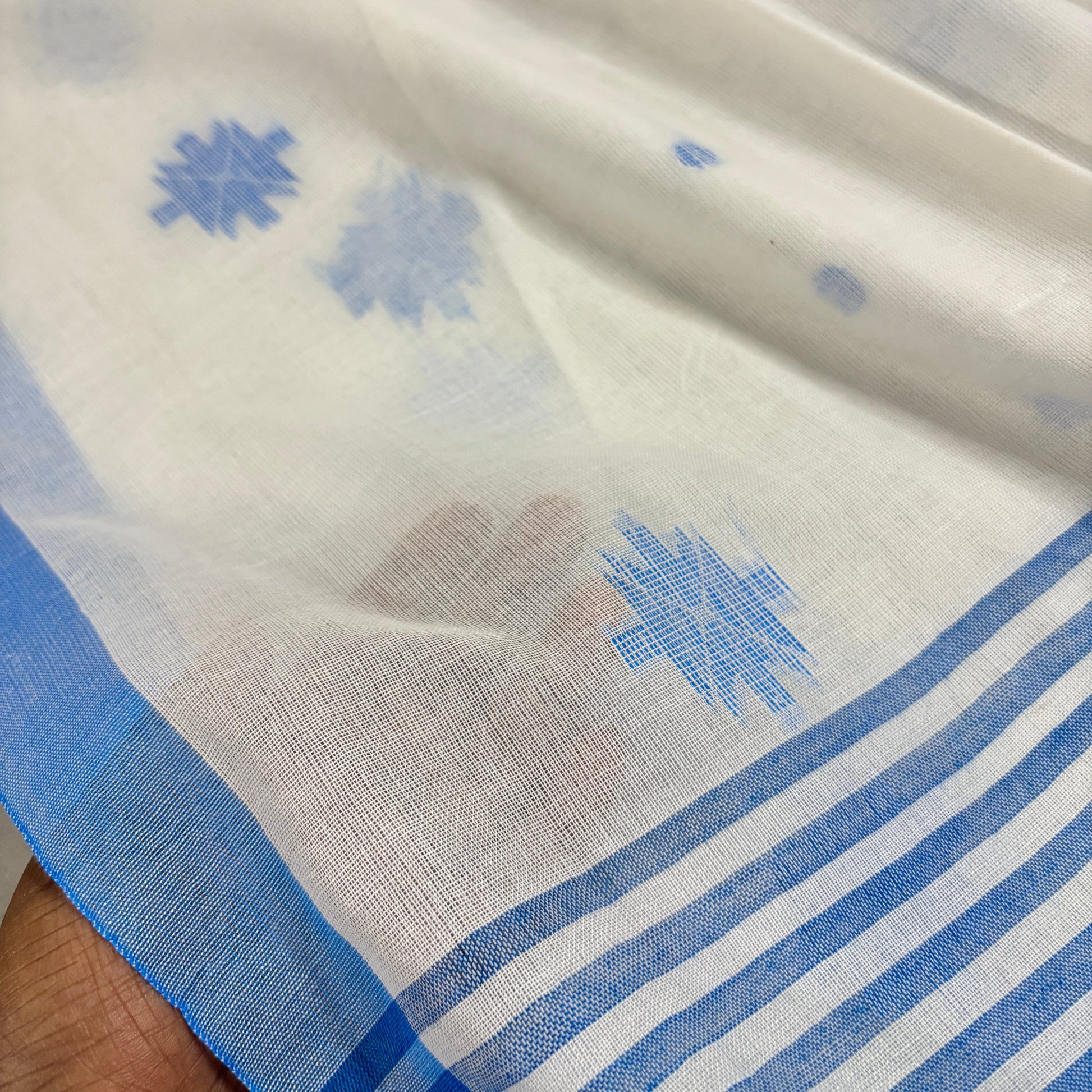 Close-up of white pure cotton saree with blue floral patterns and stripes.