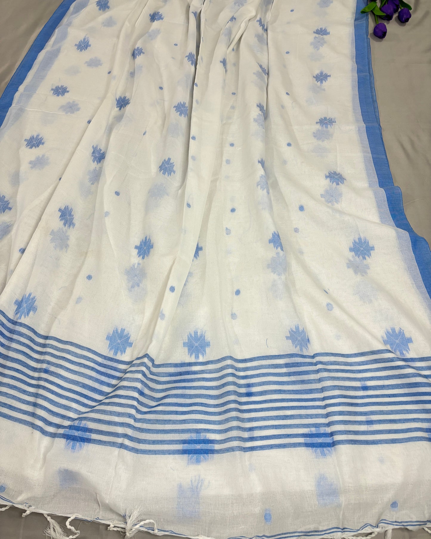 White Shuchi Label saree with blue floral patterns and stripes on pallu on a gray background