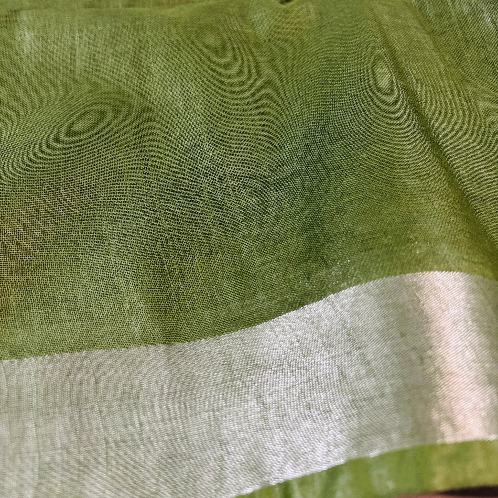 Close up of Green linen Shuchi Label saree with silver border on a white background