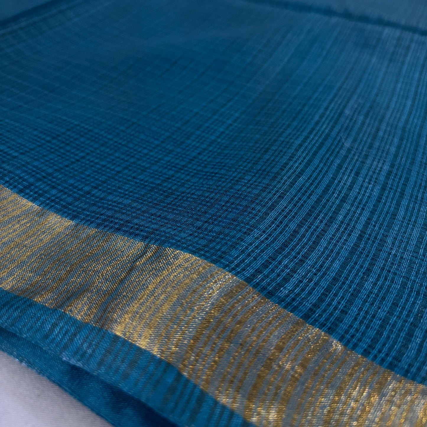 close up of Green kota doria silk saree with gold border on a grey background